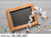 Chalkboard with measuring tape and pills on wooden background. Concept of anorexia. Стоковое фото, фотограф Pixel_shot / Фотобанк Лори