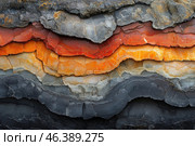 Layers of rock with vibrant hues. These layers range in color from orange and red to gray and black, creating an interesting visual effect. The geological layers in the image appear clearly defined, with texture that highlights their age and origin. Стоковое AI-изображение, AI-художник Анна Кривицкая / Фотобанк Лори