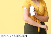 Woman with glucose sensor for measuring blood sugar level and smartphone on yellow background. Diabetes concept. Стоковое фото, фотограф Pixel_shot / Фотобанк Лори