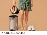 Young woman throwing high-heeled shoes into trash bin on beige background. Uncomfortable shoes concept. Стоковое фото, фотограф Pixel_shot / Фотобанк Лори