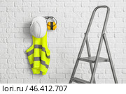 Stepladder and reflective vest with hearing protectors on white brick wall. Стоковое фото, фотограф Pixel_shot / Фотобанк Лори