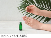 Female hands with bottle of cuticle oil and palm leaf on light background. Стоковое фото, фотограф Pixel_shot / Фотобанк Лори