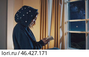 Woman reading a book near window with starry night outside. Стоковое видео, видеограф Данил Руденко / Фотобанк Лори