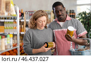 African man with European woman make choice choose consider canned pickled olives in store. Стоковое фото, фотограф Яков Филимонов / Фотобанк Лори