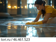 A young woman in a yellow uniform and rubber gloves, washing the floor of a large, elegant room. She is leaning over soapy water, carefully cleaning the surface. The reflection on the wet floor shows columns and soft light from the lanterns, creating an atmosphere of calm and comfort.The woman is focused on her work, her hair pulled back into a ponytail, and her facial expression conveys purposefulness. The light falls softly on her, emphasizing the details of her clothes and drops of water. The visual contrast between the shiny surface of the floor and the deep shadows in the room gives the scene an artistic quality. Стоковое AI-изображение, AI-художник Анна Кривицкая / Фотобанк Лори