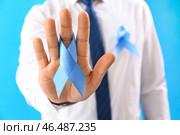 Бизнесмен с лентой осведомленности на синем фоне, крупным планом. Концепция рака простаты. Стоковое фото, фотограф Pixel_shot / Фотобанк Лори