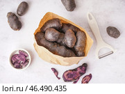 Бумажный пакет с сырым фиолетовым картофелем и овощечисткой на светлом фоне. Стоковое фото, фотограф Pixel_shot / Фотобанк Лори