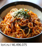 A mouth-watering dish of noodles coated in a thick tomato sauce with meat, vegetables and seasonings. The noodles are a rich reddish-orange hue and are topped with grated cheese, sliced ​​strips of nori and perhaps some herbs. The bowl is strewn with bits of mushrooms and other ingredients, adding texture and richness. The dark ceramic bowl contrasts with the bright colour of the sauce, creating a striking visual accent. Стоковое AI-изображение, AI-художник Анна Кривицкая / Фотобанк Лори
