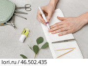 Женские руки наносят масло на кутикулу на ногтях, маникюрные инструменты и полотенце на сером грунтовом фоне. Стоковое фото, фотограф Pixel_shot / Фотобанк Лори