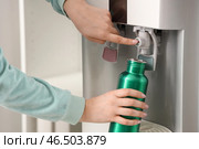 Женские руки наполняют бутылку фильтрованной водой из кулера в комнате. Стоковое фото, фотограф Pixel_shot / Фотобанк Лори