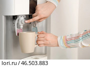 Женщина наполняет чашку фильтрованной водой из кулера возле белой стены. Стоковое фото, фотограф Pixel_shot / Фотобанк Лори