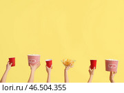 Руки держат ведра с попкорном, напитками и картофельными чипсами на желтом фоне. Стоковое фото, фотограф Pixel_shot / Фотобанк Лори