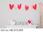 Каминная полка с надписью HOME, подарочными коробками в форме сердца и гирляндой из бумажных сердец. Празднование Дня святого Валентина. Стоковое фото, фотограф Pixel_shot / Фотобанк Лори