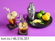Бокалы с вкусным Лонг-Айлендским айс-ти и шейкер с цитрусовыми фруктами на фиолетовом фоне. Стоковое фото, фотограф Pixel_shot / Фотобанк Лори