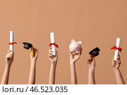 Женские руки с дипломами, копилкой и декоративными шапочками выпускников на бежевом фоне. Стоковое фото, фотограф Pixel_shot / Фотобанк Лори