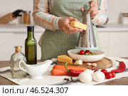 Женщина натирает сыр на пасту за столом на кухне, крупный план. Стоковое фото, фотограф Pixel_shot / Фотобанк Лори
