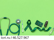 Атласная зелёная лента, стетоскоп, шприцы и таблетки на цветном фоне. Национальный месяц осведомлённости о церебральном параличе. Стоковое фото, фотограф Pixel_shot / Фотобанк Лори