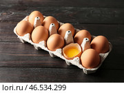 Треснутые и цельные куриные яйца в картонной упаковке на темном деревянном столе. Стоковое фото, фотограф Pixel_shot / Фотобанк Лори