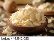 Pieces of white chocolate or cocoa butter in a wooden bowl. They look fragile, lightly dusted with white powder (possibly powdered sugar or the remains of broken pieces). Wooden utensils and warm colors create an atmosphere of coziness and naturalness. Small pieces are scattered around the bowl, and additional containers with similar contents are visible in the background. The atmosphere of the photo emphasizes the freshness, naturalness and appetizing appearance of the product. Стоковое AI-изображение, AI-художник Анна Кривицкая / Фотобанк Лори