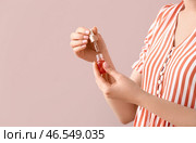 Женщина держит бутылку с маслом для кутикулы возле цветной стены. Стоковое фото, фотограф Pixel_shot / Фотобанк Лори
