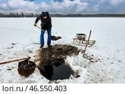 Farmer extracts sapropel sludge from freshwater lake through ice hole, he loads muck into container, using sled to haul organic fertilizer for agriculture. Стоковое фото, фотограф Владимир Григорьев / Фотобанк Лори