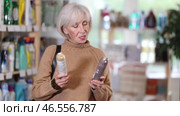 Elderly woman with gray hair choosing aerosol deodorant in household store. Стоковое видео, видеограф Яков Филимонов / Фотобанк Лори