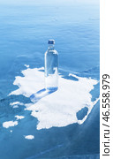 Glass bottle with cold natural drinking water stands on ice of frozen Baikal Lake on snow podium on cold winter day. Advertising and branding of drinking fresh ecological water. Nature background. Copy space. Стоковое фото, фотограф Виктория Катьянова / Фотобанк Лори