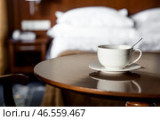 A white cup of hot tea or coffee on a wooden table in the interior of a hotel room. The concept of drinks and comfortable hotel accommodation. Стоковое фото, фотограф Photojuli / Фотобанк Лори