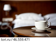 A white cup of hot tea or coffee on a wooden table in the interior of a hotel room. The concept of drinks and comfortable hotel accommodation. Стоковое фото, фотограф Photojuli / Фотобанк Лори