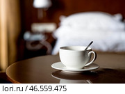 A white cup of hot tea or coffee on a wooden table in the interior of a hotel room. The concept of drinks and comfortable hotel accommodation. Стоковое фото, фотограф Photojuli / Фотобанк Лори