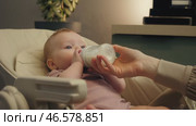 Mother Feeding Baby with Bottle in High Chair. Стоковое видео, видеограф Михаил Матвеев / Фотобанк Лори