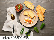 Вкусные крекеры с творогом и вареньем из перца халапеньо в тарелке на сером деревянном столе. Стоковое фото, фотограф Pixel_shot / Фотобанк Лори