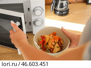 Женщина ставит миску с вкусной едой в современную микроволновую печь на деревянном столе. Стоковое фото, фотограф Pixel_shot / Фотобанк Лори