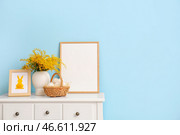 Корзина с пасхальными яйцами, цветами мимозы и пустой фоторамкой на столе возле цветной стены. Стоковое фото, фотограф Pixel_shot / Фотобанк Лори