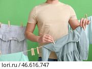 Молодой человек вешает детское платье на прищепках на зеленом фоне, крупным планом. Стоковое фото, фотограф Pixel_shot / Фотобанк Лори