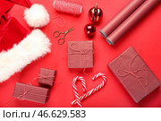 Композиция с подарочными коробками, оберточной бумагой и шапкой Санты на красном фоне. Стоковое фото, фотограф Pixel_shot / Фотобанк Лори