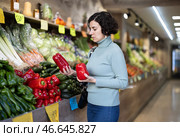 Woman carefully selects red bell peppers in grocery supermarket. Стоковое фото, фотограф Яков Филимонов / Фотобанк Лори