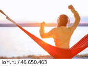 Молодая женщина слушает музыку, отдыхая в гамаке на открытом воздухе. Стоковое фото, фотограф Pixel_shot / Фотобанк Лори