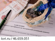 Бланк заявления о выдаче государственного сертификата на материнский (семейный) капитал, ручка, игрушечная люлька с монетами и пачка банкнот номиналом 5000 российских рублей. Стоковое фото, фотограф Сергей Елагин/Бизнес Online / ТАСС / Фотобанк Лори