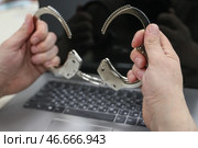 Наручники в руках интернет-мошенника на фоне ноутбука. Стоковое фото, фотограф Сергей Булкин/NEWS.ru / ТАСС / Фотобанк Лори