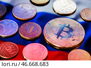Монета криптовалюты биткойн в окружении монет российского рубля различного достоинства на фоне российского флага. Стоковое фото, фотограф Сергей Елагин/Бизнес Online / ТАСС / Фотобанк Лори