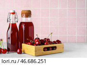 Бутылки сладкого вишневого ликера и деревянный ящик с свежими ягодами на белом столе. Стоковое фото, фотограф Pixel_shot / Фотобанк Лори