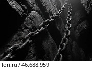 Massive metal chains hanging along a rough stone wall in a dark, narrow space. The atmosphere of the image is dark, with an emphasis on the texture of rusty metal and wet stone. The light falls from the top of the image, creating a contrast between light and shadow, emphasizing the harshness of the scene. The black and white palette adds drama and enhances the feeling of mystery and abandonment. Стоковое AI-изображение, AI-художник Анна Кривицкая / Фотобанк Лори