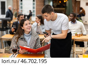 On open area of cafe, guy waiter communicates with girl customer, accepts order. Стоковое фото, фотограф Яков Филимонов / Фотобанк Лори