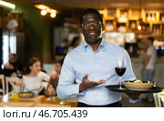 African man of public catering cafe carries order to client, ready to serve guest of cafe establishment. Стоковое фото, фотограф Яков Филимонов / Фотобанк Лори