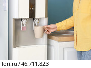 Женщина наполняет чашку фильтрованной водой из кулера рядом с синей стеной. Стоковое фото, фотограф Pixel_shot / Фотобанк Лори