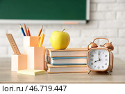 Яблоко, книги, будильник и канцелярские принадлежности на учительском столе в классе. Концепция возвращения в школу. Стоковое фото, фотограф Pixel_shot / Фотобанк Лори