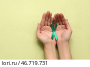 Женские руки держат зелёную ленту на цветном фоне. Национальный месяц осведомлённости о церебральном параличе. Стоковое фото, фотограф Pixel_shot / Фотобанк Лори