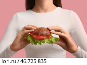 Женщина держит вкусный бургер с пластиком на розовом фоне, крупный план. Месяц осведомленности о микропластике. Стоковое фото, фотограф Pixel_shot / Фотобанк Лори