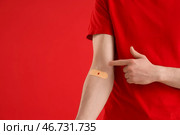 Мужчина-донор крови указывает на наложенный пластырь на красном фоне, крупный план. Стоковое фото, фотограф Pixel_shot / Фотобанк Лори